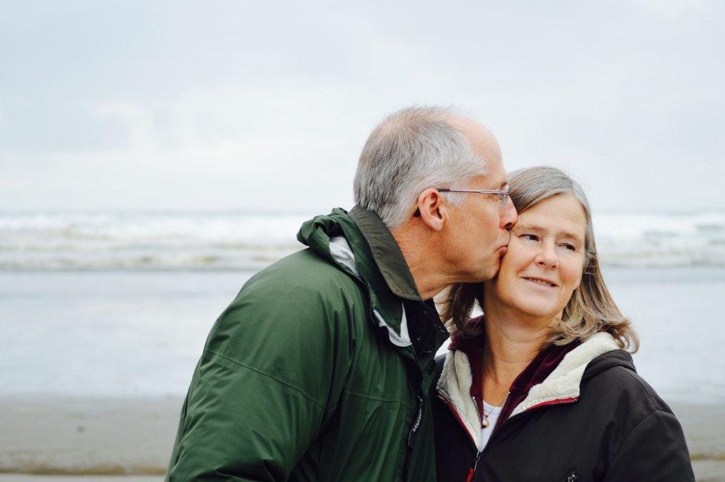 Photo of an older couple kissing on the cheek.