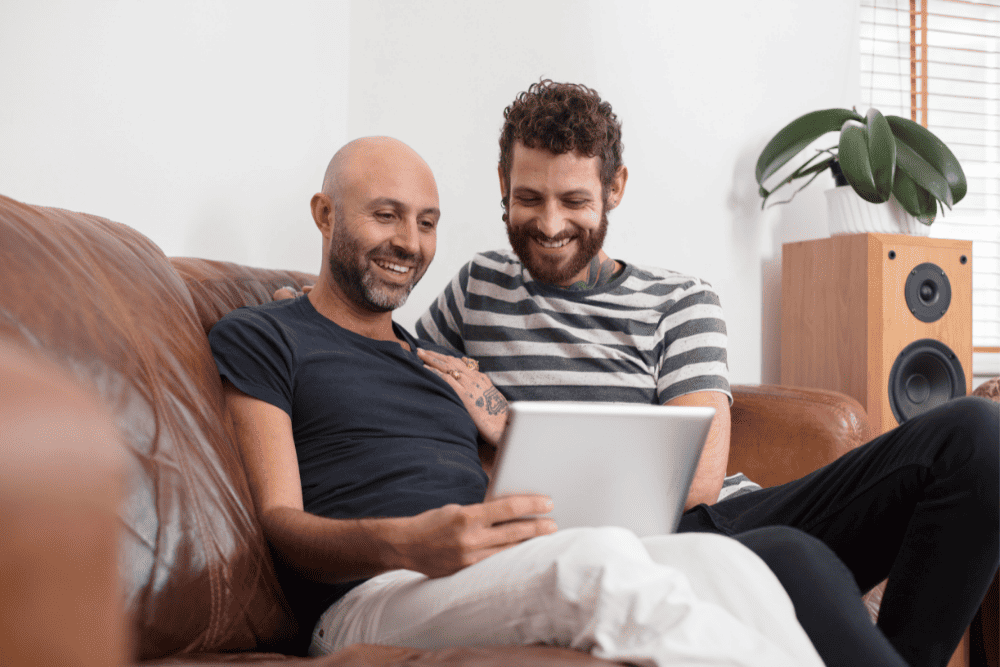 Photo of a LGBTQ couple holding a tablet to talk with their couples therapist during a therapy session. This represents how online therapy in NC an VA can help couples feel comfortable and safe to explore their issues and work on the relationship together.