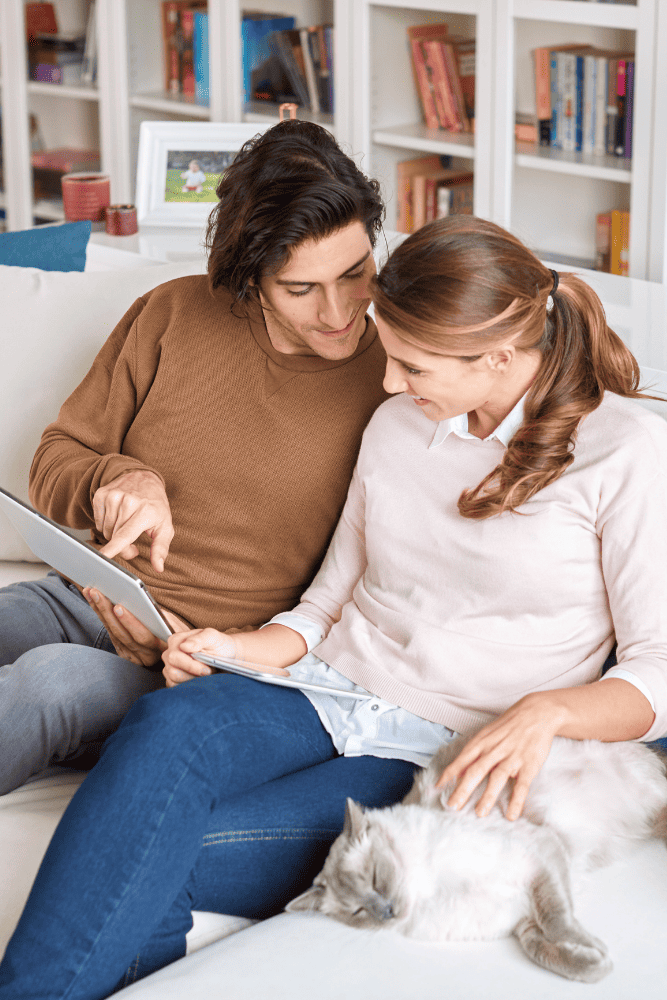 Photo of a couple sitting on their couch and holding a tablet looking for a online therapist. This represents how online counseling in NC and VA can help you get the support you need from the comfort of your own home.