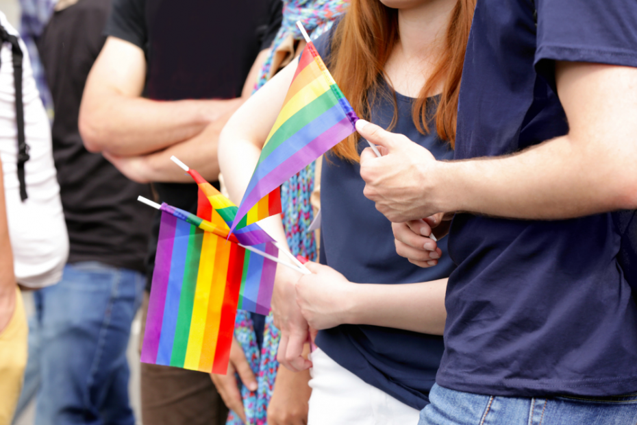 Photo of a group of people holding LGBTQ+ flags celebrating Pride. This represents how therapy for LGBTQ+ individuals and couples can help achieve self-acceptance, embrace your identity and find happiness.