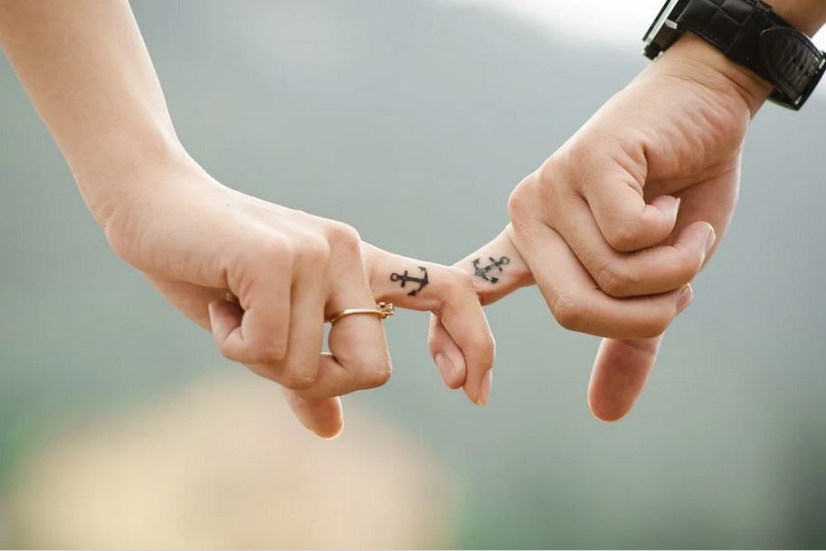 Photo of a married couple with matching anchor tattoos with their fingers intertwined. This represents how marriage counseling can help you and your partner overcome your issues together.