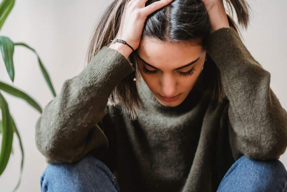 Photo of a woman holding her head in her hands, with a worried look. A powerful tool you can use against anxiety starts with this: stop comparing yourself to others.