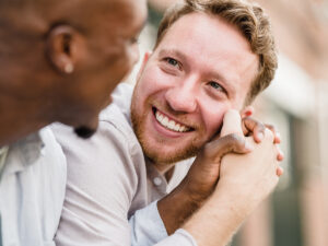 Photo of a LGBTQ couple holding each other hand and looking in each others' eyes with a loving expression. This represents how couples therapy is worth it when you're looking to work on your relationship and invest in your happiness.